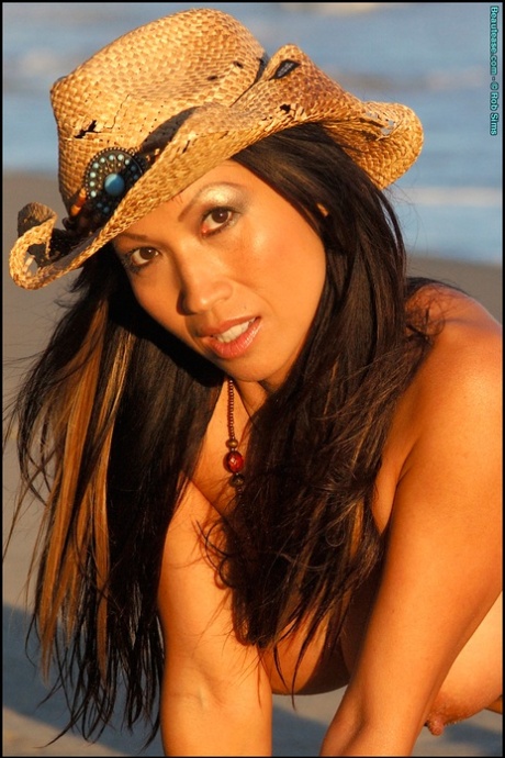 Rossie Cottrell, a well-known Asian model, displays her firm buttocks on the beach wearing a straw hat.