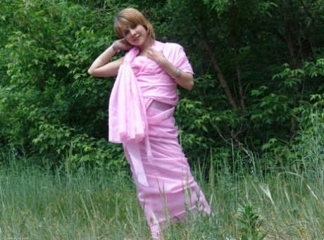 A young competitor named Liza is seen naked in a field located near the line of trees.