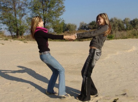 While at the beach, young girls wearing denim jeans and jackets hold hands in bare skin.