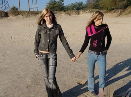 While at the beach, young girls dressed in denim jeans and jackets hold hands without clothing.