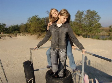 At the beach, young girls wearing denim jeans and jackets hold hands in bare skin.