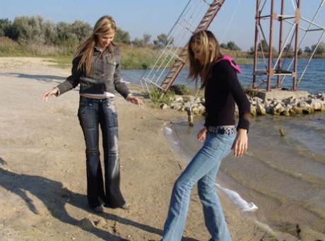 Denim jeans and jackets are worn by young girls who hold hands while at the beach without nudity.