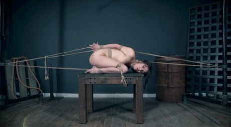 A helpless brunette named Alex More screams in agony while being held back by ropes.