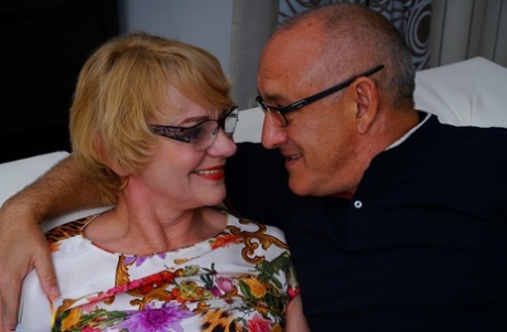 Husband delights in a playful moment as his wife, who is wearing glasses, seduces him with her mouth and hot dog.