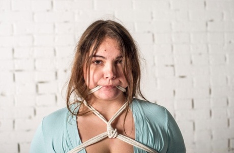 White BBW slave girl tied up with rope, feet off and big breasts on show.
