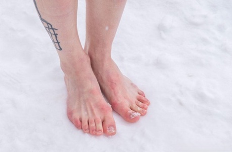 In the snow, a girl with tattooed feet is forced to kneel and stand barefoot due to her condition.