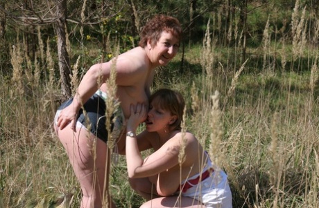 A lesbian woman and a mature woman play in a field while playing with each other.