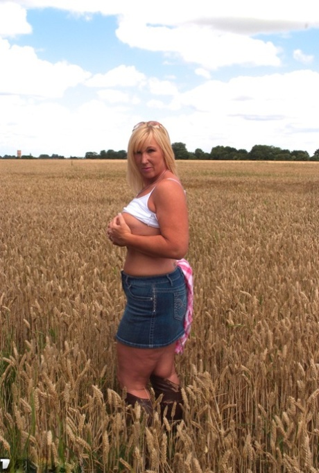 MILF Melody, a chubby and fully developed female, displays impressive big tits and flashes her buttocks in a field.