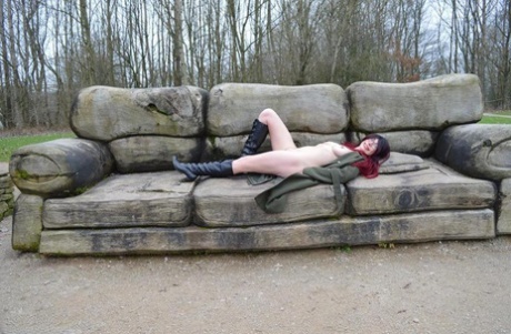 In a jacket and boots, BarbySlut is an adult redhead who exudes attractiveness while lying naked outside.