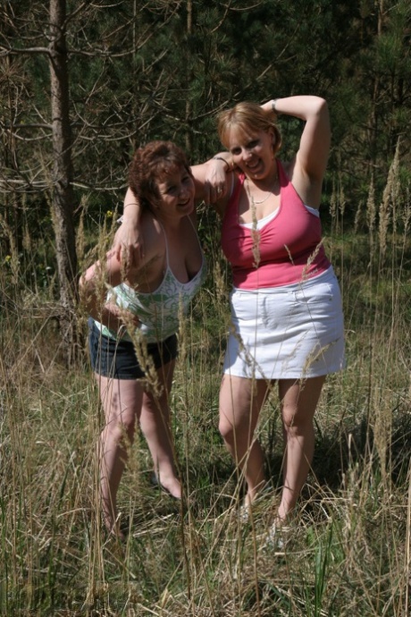 Large tits are revealed by older woman Kinky Carol and her girlfriend as they pose next to trees.