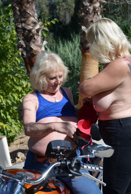 The older, blonde lesbians ride a motorcycle outside without a top.