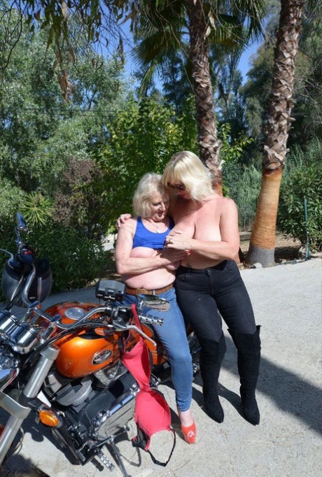 Aged lesbians who are blonde leave their tops on while riding a motorcycle in the open air.