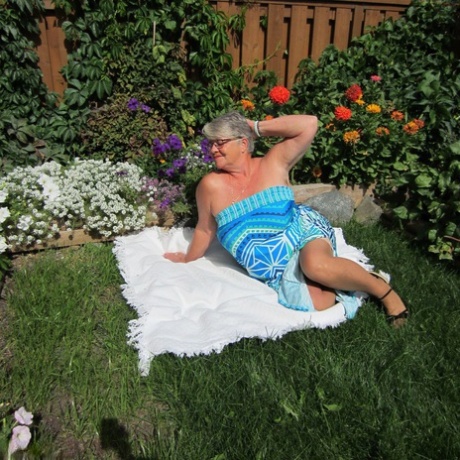 The Girdle Goddess, the fat nan, exposes herself to sheer pantyhose on a blanket by a flower bed.
