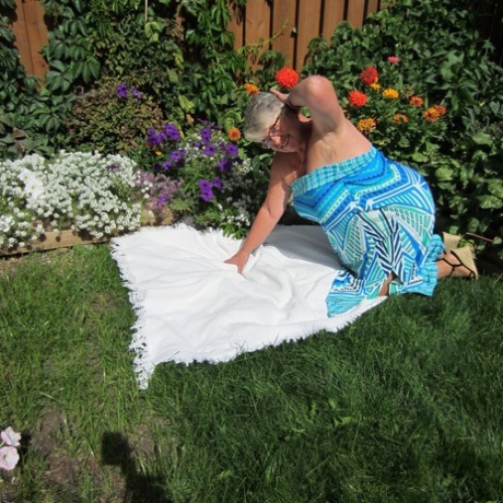 Fat nan Girdle Goddess exposes herself to sheer pantyhose on the blanket by a flower bed.