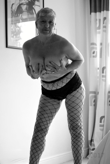 With short hair and floppy legs, an elderly woman wears fishnet pantyhose and sports a strapon.
