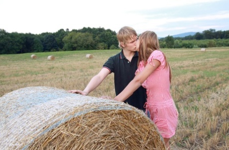 A young couple engage in sexual activity with a round bale in a farmer's field.