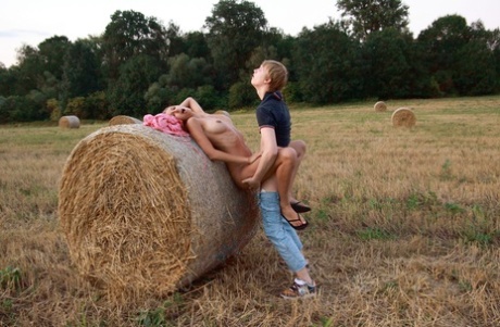 In a farmers field, a young couple engages in sexual activity by beating up a round bale.