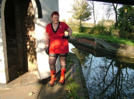 Valgasmic Exposed, a mature redhead who is wearing punk boots, exposes herself on the footbridge.