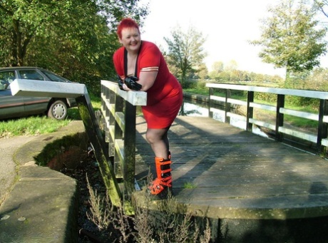 Aged red, Valgasmic Exposed bares her feet on a footbridge while wearing punk boots.