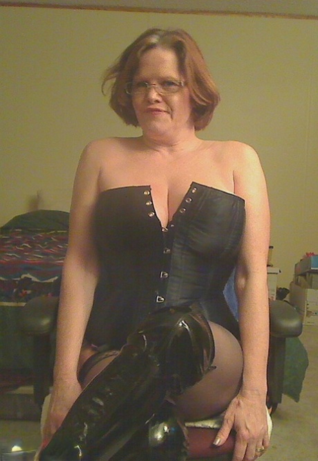 Redheaded amateur Misha MILF releases her large tits from a corset in OTK boots.