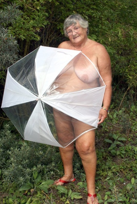 Posing naked by fir trees, Obese oma Grandma Libby holds an umbrella.