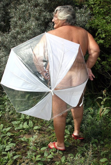 While posing naked by the fir trees, Obese oma Grandma Libby holds an umbrella in her hands.
