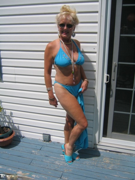 A healthy blonde woman named Ruth releases her thighs and buttocks from a bikini while wearing sunglasses.