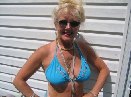 Ruth, the mature blonde, removes her clothing from a bikini while wearing sunglasses to release her inner tubes and buttocks.