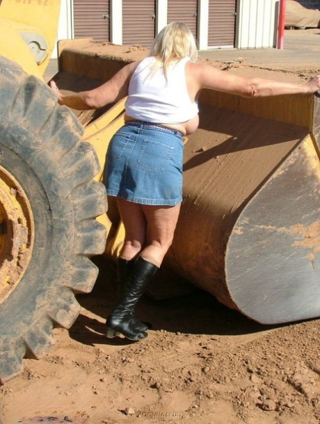 Adonna, who is an overweight and mature blonde, takes on heavy equipment while standing in front of it.