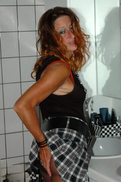 Kyras Nylons, an adult who is freched and brunette, laces herself with her skirt in the bathroom while wearing pantyhose.