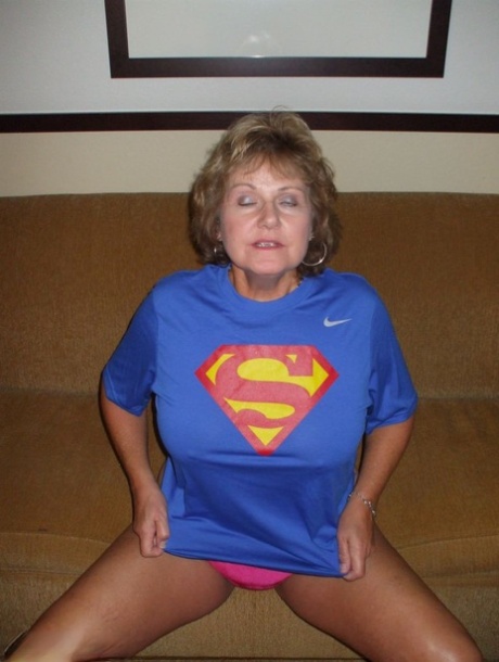 Busty Bliss, an older woman, removes her large boobs from a Superman T-shirt.