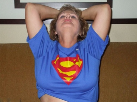 An older woman named Busty Bliss removes her large boobs from a Superman T-shirt.