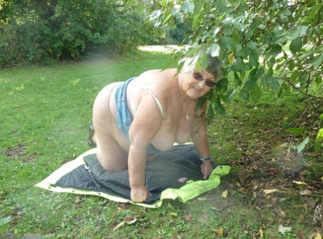 Grandma Libby, who is overweight and British, stands before a tree in a park.