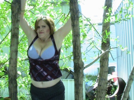 Thick, older woman Misha MILF stands and basks in a cluster of tall hardwood trees.