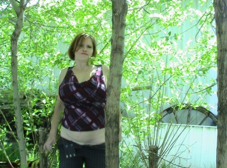 Misha MILF, a tall woman of substantial age, is seen sitting in a group of hardwood trees.