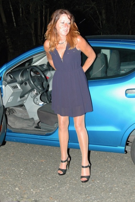 Kyras Nylons, a young woman, displays a breast by using the hose outside her car at night.