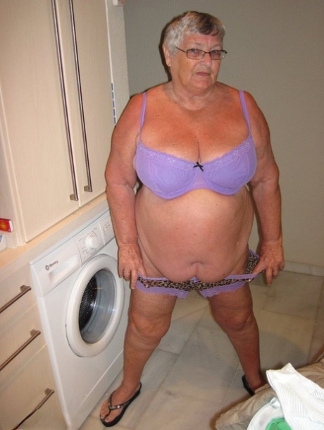 The excess weight of Grandma Libby, a British woman with ample height and great physique, exposes her breast tissue while ironing.