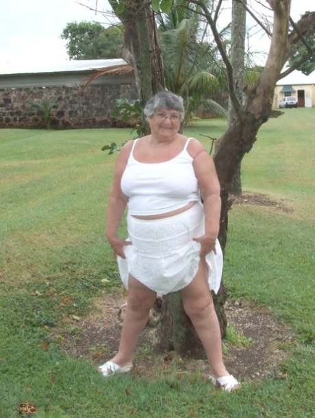 An obese British woman named Grandma Libby displays her large breasts beneath a tree.