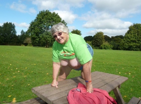 On a picnic table, Grandma Libby exposes her large breasts and buttocks, which are visible in the image of an obstructed woman.