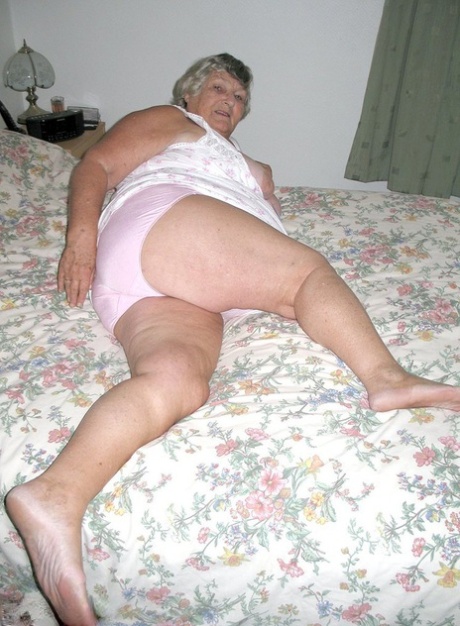 After being naked on a bed, Grandmama Libby takes hold of her fat roll.