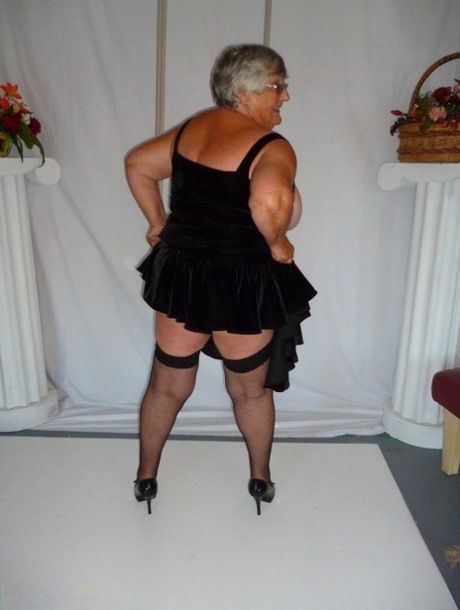 Grandma Libby, who is fat, removes her clothing from a black dress and models herself in stockings.