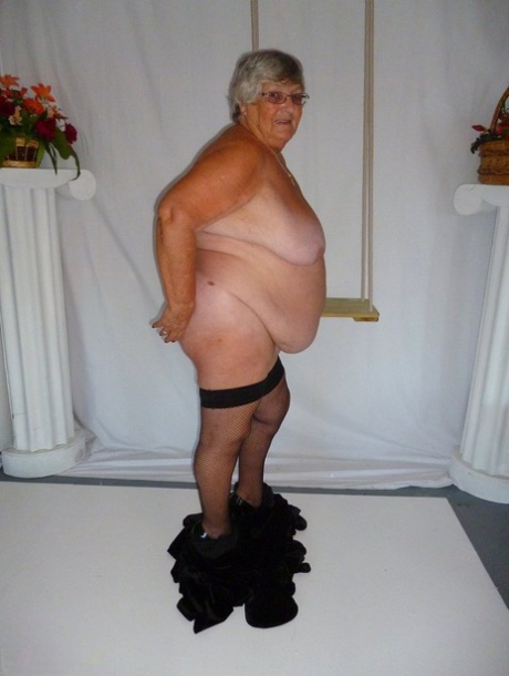 Wearing a black dress and stockings, Grandma Libby poses for the camera in a nude picture.