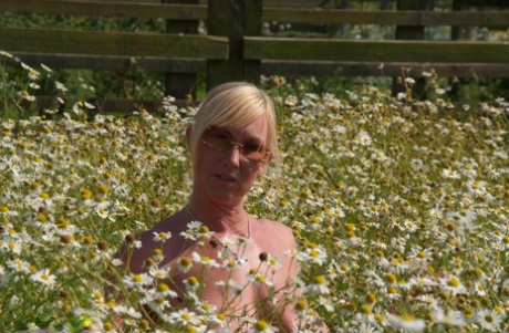 Blonde Melody, who is overweight and has a tall build, removes her breasts in front of wild flowers in a field.