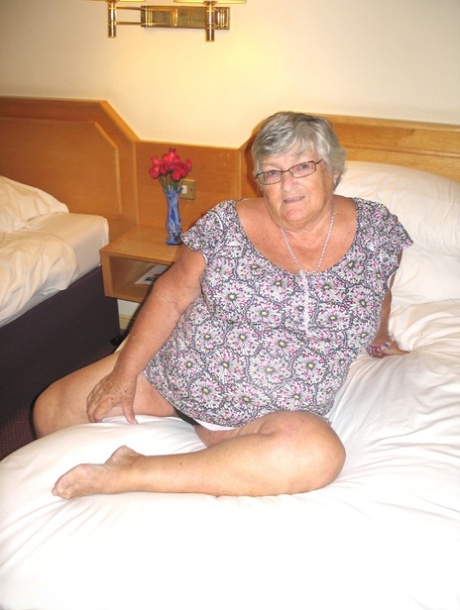 On a bed, Grandma Libby, an overweight woman with silver hair, exposes her fat body.
