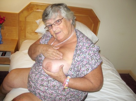 A silver-haired British woman, Grandma Libby, exposes her plump physique on a bed.