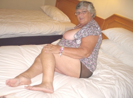 Grandma Libby, who is an attractive silver-haired British woman, displays her excess body fat on the bed.