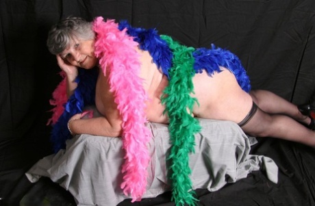 Grandma Libby, who is fat and shows her big tits while wearing feather boas, poses for a photo.