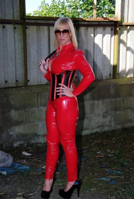 While unzipping red latex attire, Melody, a seductive and mature blonde, wields a whip.