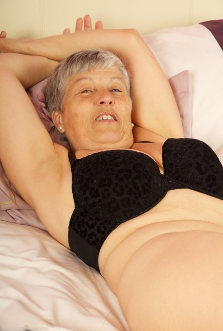 A thong-like British woman known for her short hair exposes herself on a bed, revealing her big breasts.