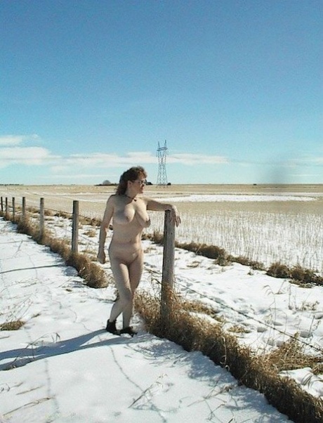 On a snowy terrain, Misha MILF stands as a mature amateur and is stripped down.